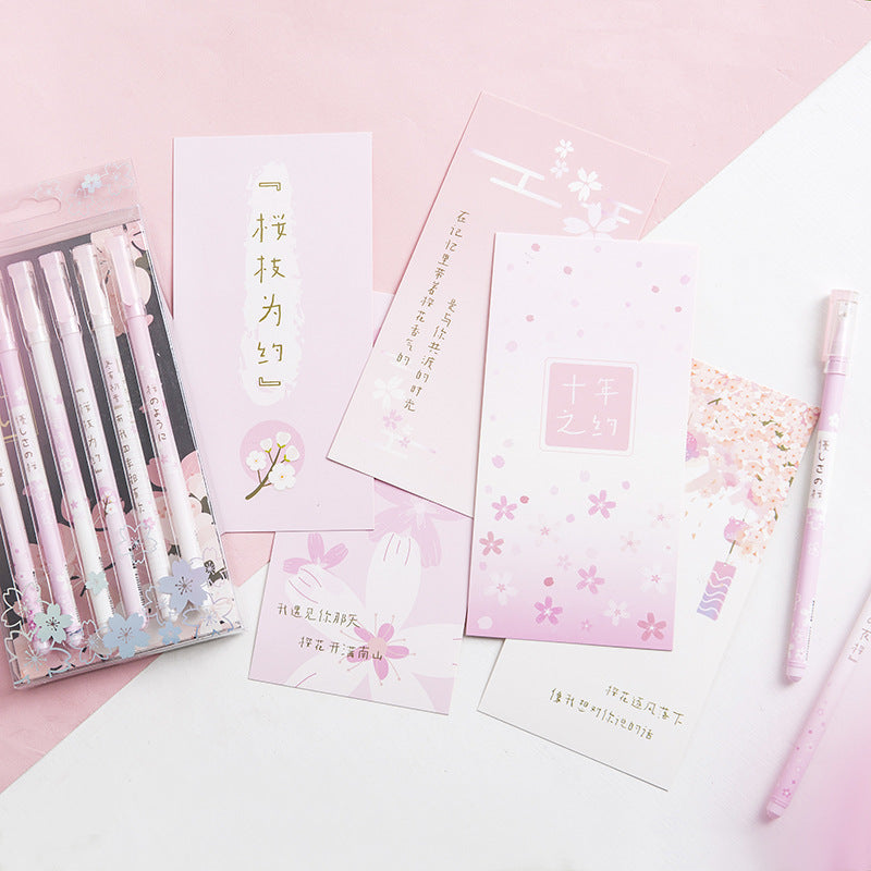 Set of stationery items including pens and cards with floral designs on a pink background