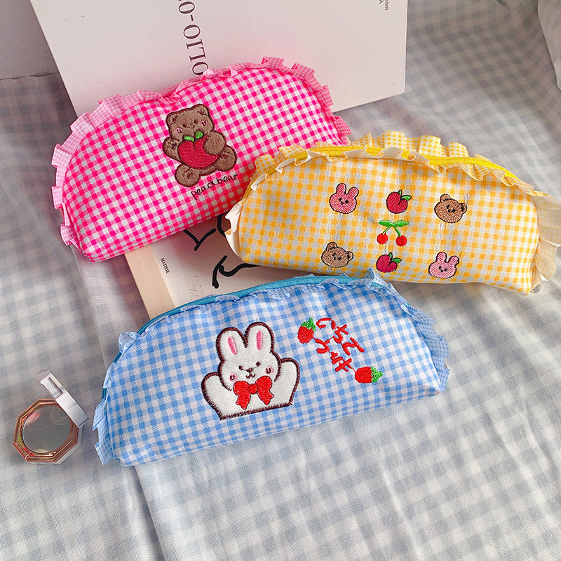 Three colorful gingham pouches with embroidered designs on a checkered surface.