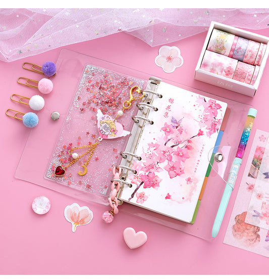 Decorative stationery items including a planner, stickers, and clips on a pink background