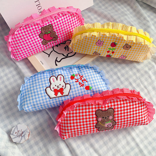 Four colorful gingham pencil cases with embroidered designs on a checkered background.