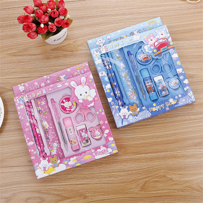 Two stationery sets, one pink and one blue, on a wooden surface with a small potted plant.
