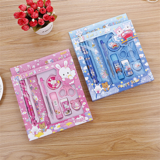 Two stationery sets, one pink and one blue, on a wooden surface with a small potted plant.
